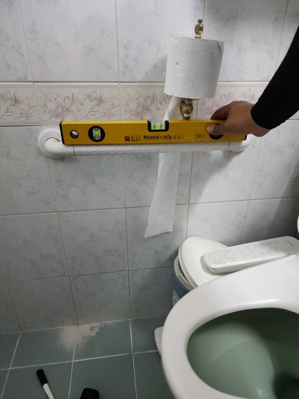 변기 옆에 설치한 흰 안전바에 수평자를 대는 모습