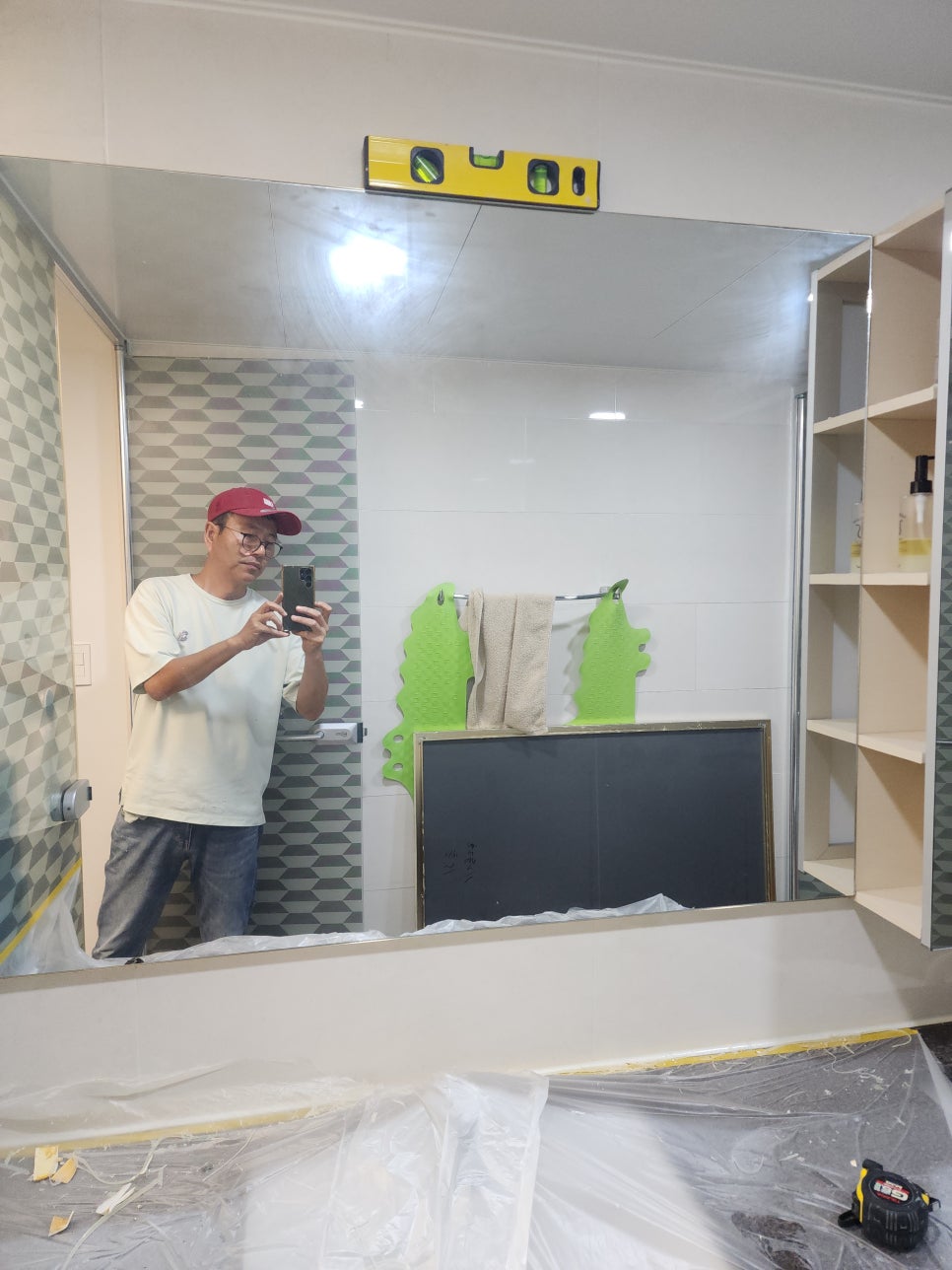 새 욕실 거울 상단에 수평계를 올려 확인하는 모습