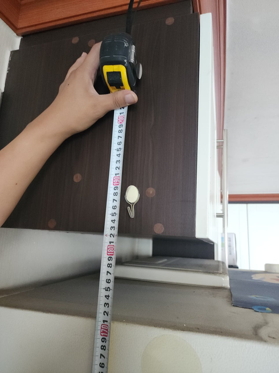 냉장고 위 상부장과 냉장고 사이 간격을 줄자로 측정하는 모습