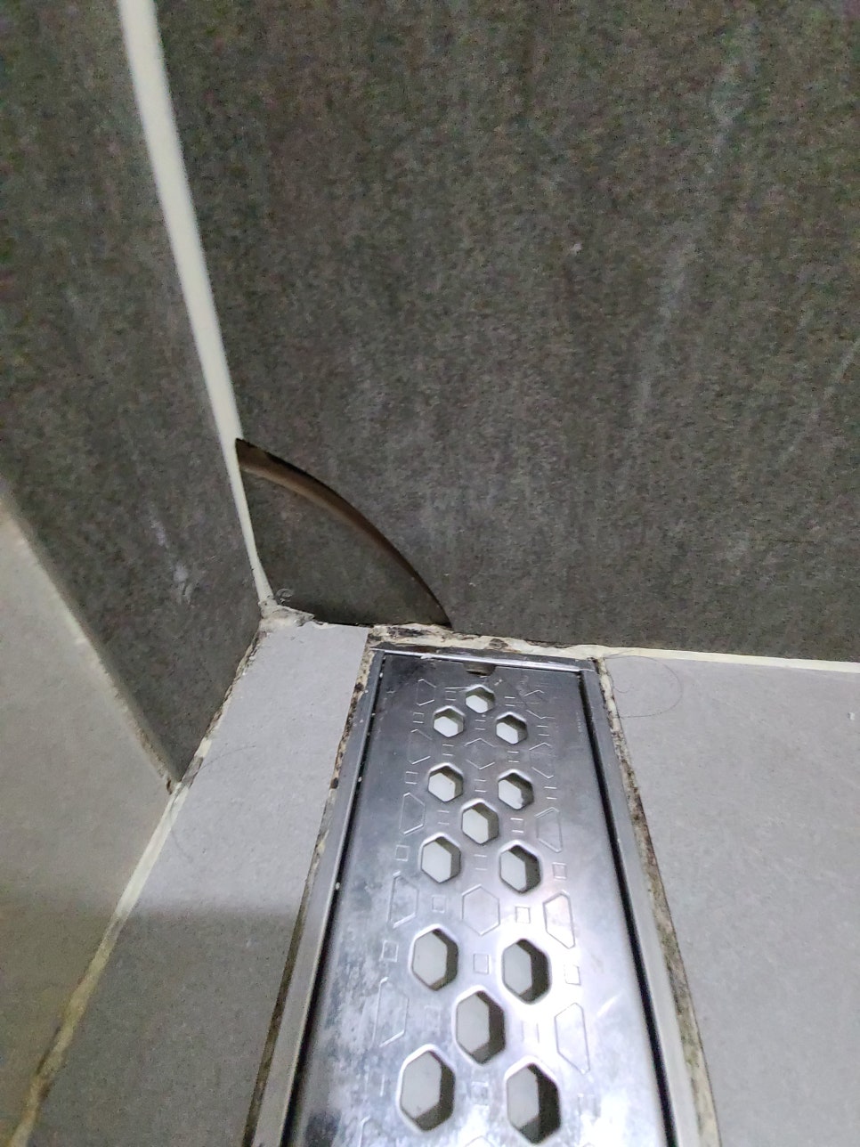 배수구 옆 벽면에서 한 장이 깨진 회색 타일