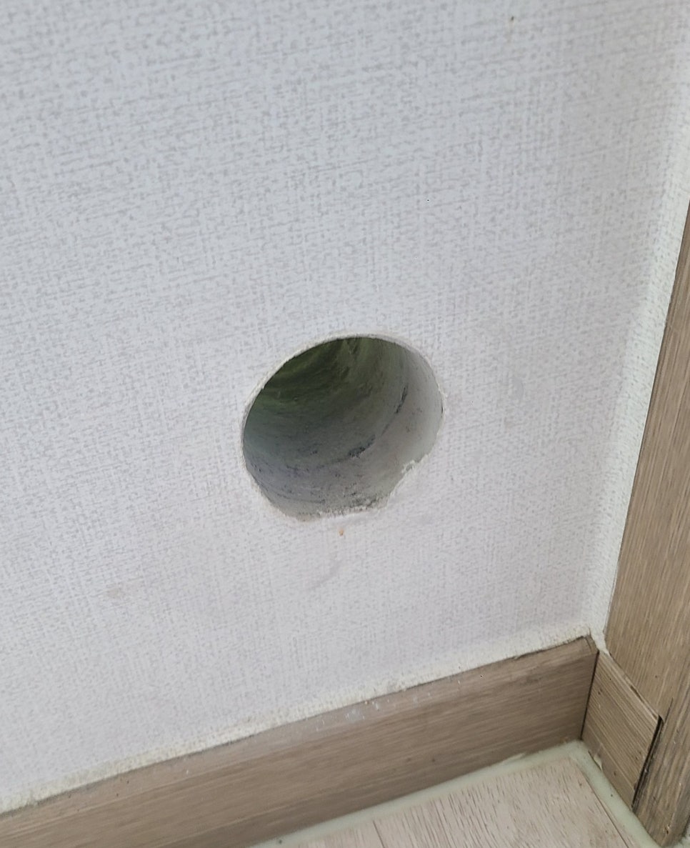 실내 벽지 아래쪽에 남아 있는 원형 에어컨 배관 구멍