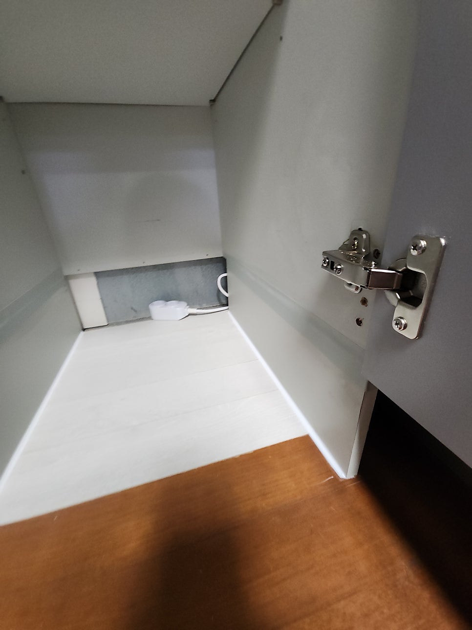 흰색 마감 바닥과 문짝 경첩 옆으로 충전 배선이 놓인 하부장 내부